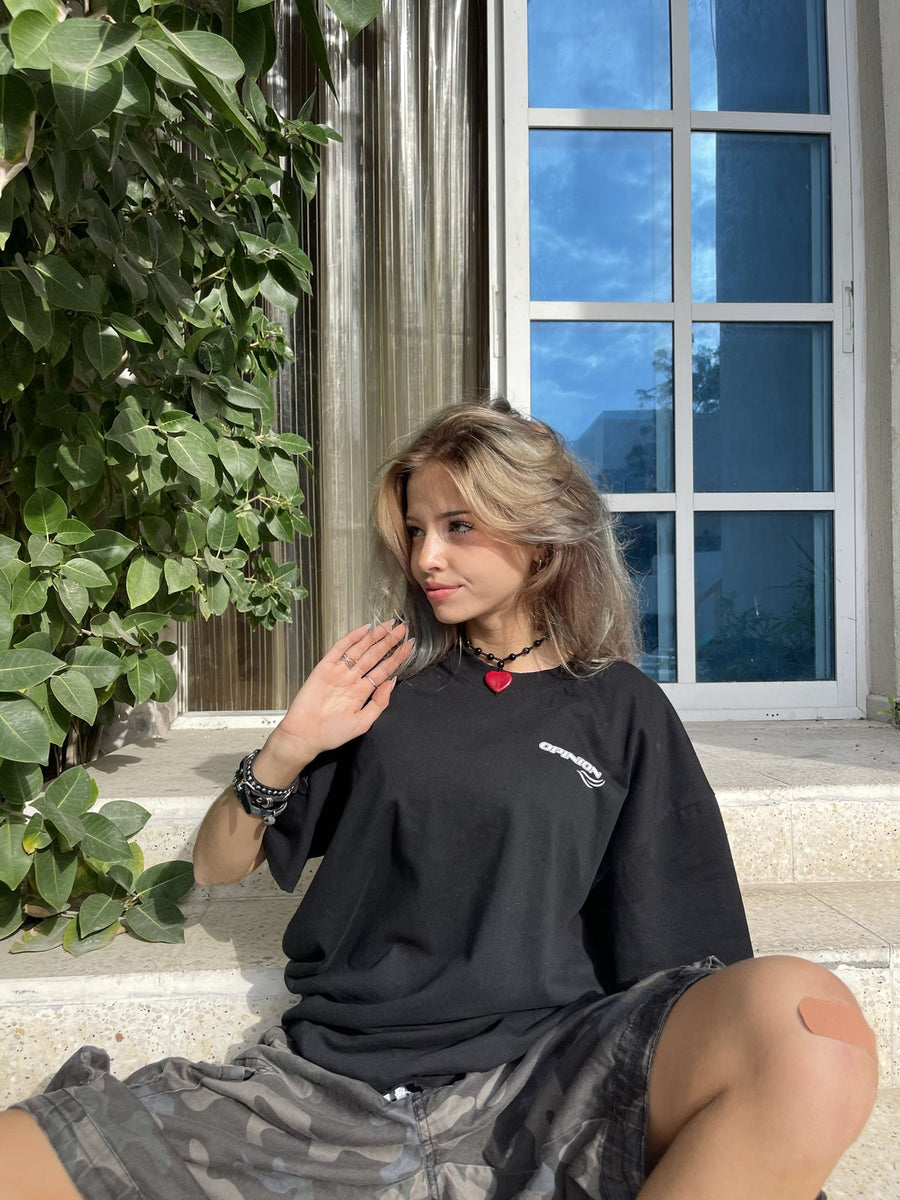 Model sitting on steps in the black Past x Future tee, front logo
